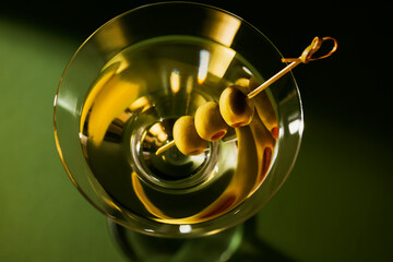 Glass of classic dry martini cocktail with olives on dark green background.