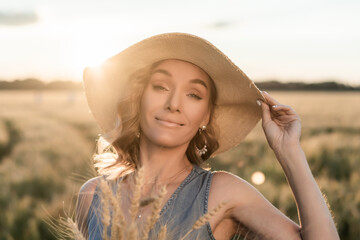 Girl in a wide-brimmed hat on a wheat field in the rays of the setting sun