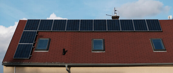Red tile roof of home with modern roof windows and solar panels. Eco-friendly alternative energy...