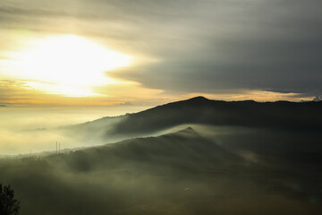 Misty valley at warm sunrise on a cloudy sky background