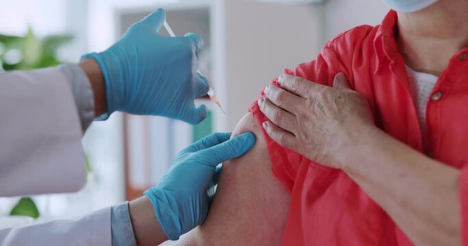 Old caucasian senior woman having doctor appointment in laboratory office. Young doctor injecting vaccination against covid-19 infection.