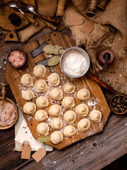 homemade dumplings with meat on rustic wooden board and table with flour, sackcloth