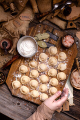 homemade dumplings with meat on rustic wooden board and table with flour, sackcloth