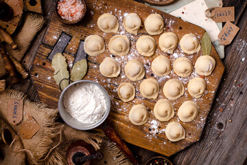 Fototapeta na wymiar homemade dumplings with meat on rustic wooden board and table with flour, sackcloth