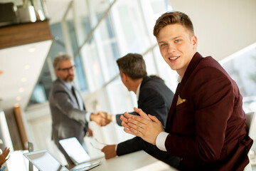 Young man clapping hands after successful business meeting in the modern office