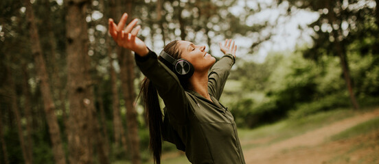 Young woman with earphones preading her arms in the forest because she enjoys training outside