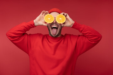 Photo of happy man with beard in red clothing covered eyes with orange fun tongue out, isolated over red background