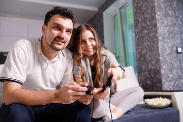 Young couple playing video games sitting on sofa in livingroom at home