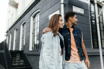 Fototapeta premium Lovers wearing the casual style looking to the side while standing in front of blurred building. Couple in love in the city. Urban lovestory