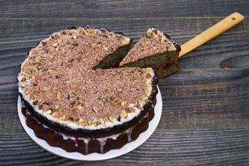 Chocolate cake decorated with grated chocolate with walnuts and a cut piece on a bamboo spatula with fruit filling.