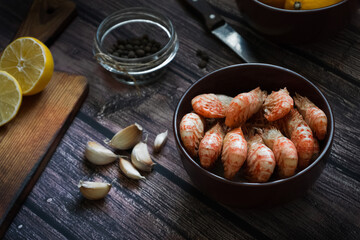 Boiled Greenlandic prawns with spices, garlic and lemon on a wooden background. Preparing a seafood dinner. A quick and healthy dinner.Rustic style