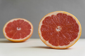 Naklejka na ściany i meble Slicing fresh organic pink grapefruit on a gray background close-up. Eating grapefruit reduces cholesterol levels in the blood and promotes weight loss. Dietary nutrition. Minimalist composition
