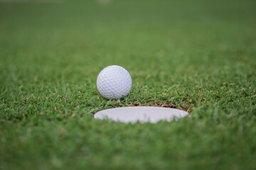 The ball at the hole on the golf course. Golf ball putting on green grass near hole golf to win in game at golf course with blur background.