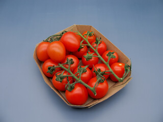 Red ripe fresh small cherry tomatoes on a branch in a cardboard tray.