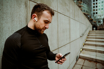 Caucasian male athlete changing music on smartphone while on outdoor run in city