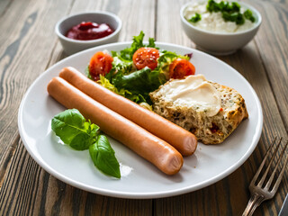 Breakfast - boiled sausages, cottage cheese, bun with mayonnaise and fresh vegetables served on wooden table
