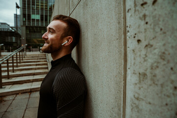 Caucasian male athlete taking a break while on outdoor run in city listening to music with earphones