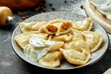 Ukrainian or Polish traditional dish - Pierogi or Varenyky (dumplings) with stuffed with cabbage and sour cream on a dark background. Close up, selective focus