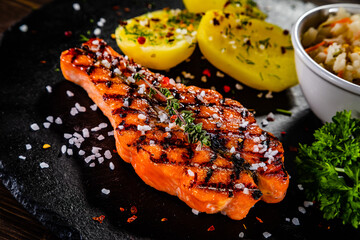 Fried salmon butterfly steak with boiled potatoes, white cabbage and parsley served on black plate on wooden table
