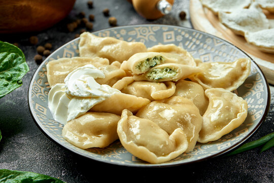 Ukrainian or Polish traditional dish - Pierogi or Varenyky (dumplings) stuffed with spinach and cheese and sour cream on a dark background. Close up, selective focus