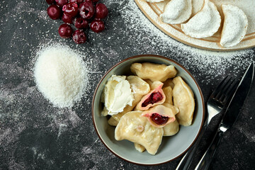Ukrainian or Polish traditional dish - Pierogi or Varenyky (dumplings) stuffed with cherry and sour cream on a dark background. Close up, selective focus
