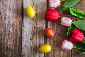 Pink and red tulips and Easter eggs on a brown wooden background. Spring background. Background for design. Copy space. Easter.