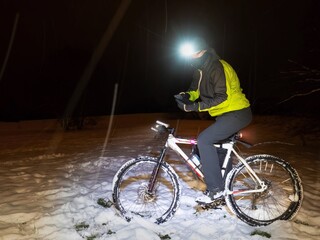 Biker checks the position in the phone. Winter snowy night.
