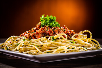 Spaghetti with marinara sauce, meat and parmesan on wooden table against gradient orange background
