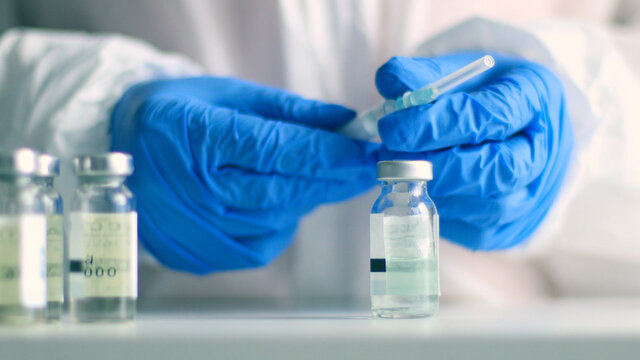 Nurse or doctor in medical protective uniform and latex rubber fill in syringe with medicine from glass vial while preparing for work during coronavirus, flu or measles pandemic for poster, web banner