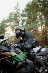 Fototapeta na wymiar Motorcyclist in a helmet on a motorcycle on a country road. Guy driving a bike during a trip. Riding a modern sports motorcycle on the highway