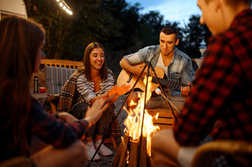 Friends playing on guitar by the bonfire, camping