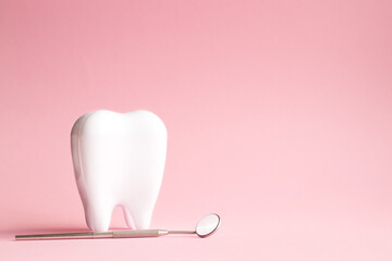 White tooth with dental mirror on pink background in honor of international dentist day with place...