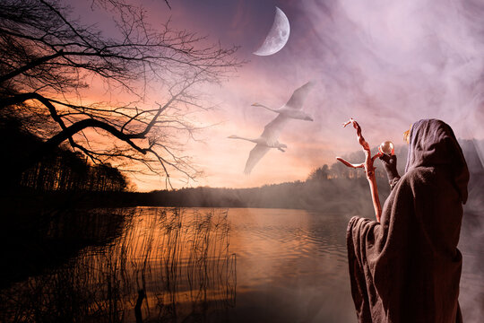 Eine fantasievolle, mystische Landschaft mit einem See, fliegenden Schw&auml;nen und einem gro&szlig;en Mond. Im Vordergrund steht eine Hexe.