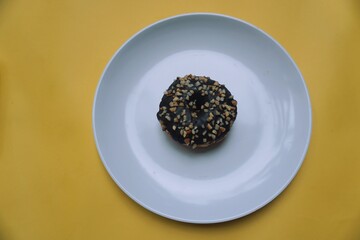 Chocolate bean donut on plate on yellow background.