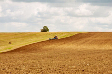 A tractor with a large plow plows a hilly field. Tractor with agricultural equipment.