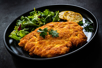 Breaded fried pork chop and fresh vegetables on black table


