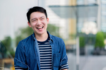 smart asian male wear casual cloth standing next to budiling facade window glasses smiling wide mouth with happiness sincerely confident emotion