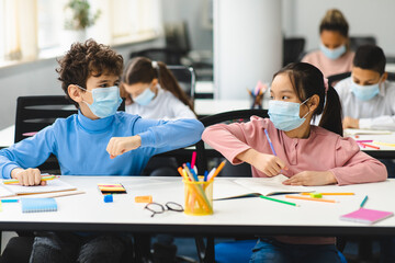 Diverse pupils wearing surgical face masks greeting and bumping elbows