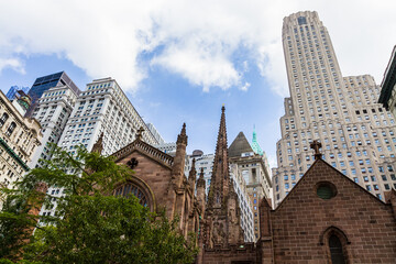 View of the top part of Trinity Church in Financial District in New York with buildings in the background and cloudy blue sky