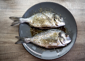 raw dorado fish on a plate sprinkled with spices before cooking by the chef