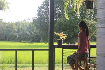 An Asian girl sits on a chair on the balcony, looking at the fields