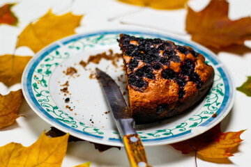 Defocus close up piece of chocolate cake on a white plate with blue ornate patterns. Brownie. Cake. White background with checkered scarf. Knife. Crumbs. Disorderly. Blueberry pie. Out of focus