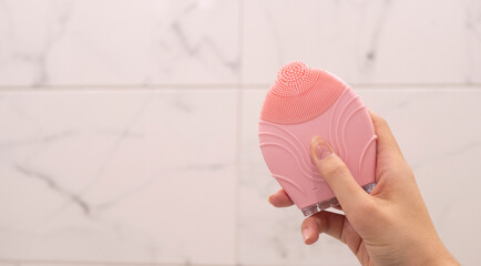 Silicon pink electronic rubber in woman hand on white marble background. Beauty care routine in...