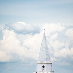 Biała wieża kościoła na tle białych obłoków na niebie