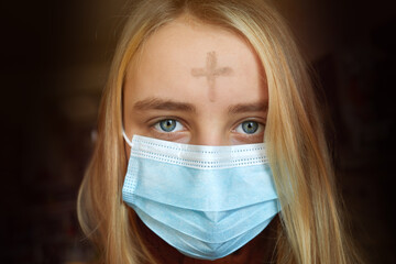 Girl with cross made from ash on forehead with face mask. Ash wednesday concept.