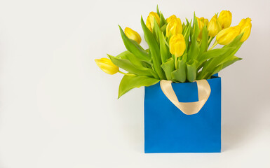 Yellow tulips in a gift bag on a white background. Postcard for March 8, Mother's Day, birthday. Flower delivery. Flower Shop. Space for text
