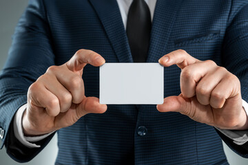 Fototapeta premium A man in a suit hands close-up shows a business card. mockup, layout. Concept for networking, business dating, important connections. Shot on a gray background.