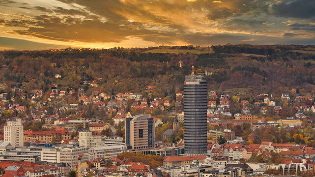Panorama von Jena bei goldenem Sonnenuntergang mit dem markanten JenTower und herbstlich bewaldeten H&auml;ngen des Saaletals, Stadtansicht in warmem Abendlicht, Jena, Th&uuml;ringen, Deutschland
