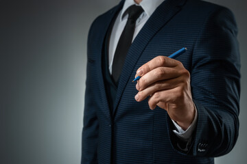 A man in a business suit holds out his hand with a ballpoint pen, writes in the air. Stock for business concept. Close-up, copy space.
