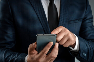 A businessman in a business suit holds a smartphone in his hands. Uses the Internet to work and communicate with partners. Online business concept, remote work, freelance. Close-up.